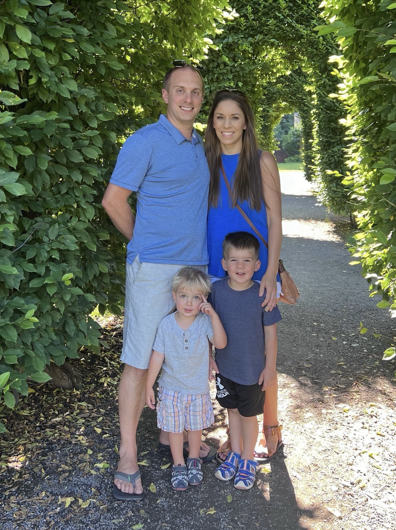 Family wearing blue t-shirts. Father is on the left and mother with long brown hair is on the right. Two young boys stand in front of their parents.
